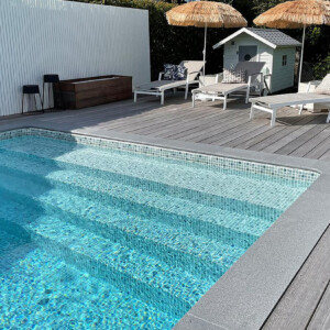 Pool med gaveltrappa och poolkant, solstolar och parasoll och ett litet poolhus