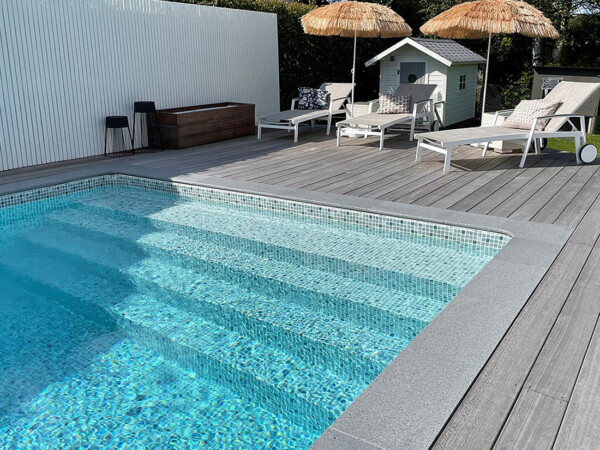 Pool med gaveltrappa och poolkant, solstolar och parasoll och ett litet poolhus